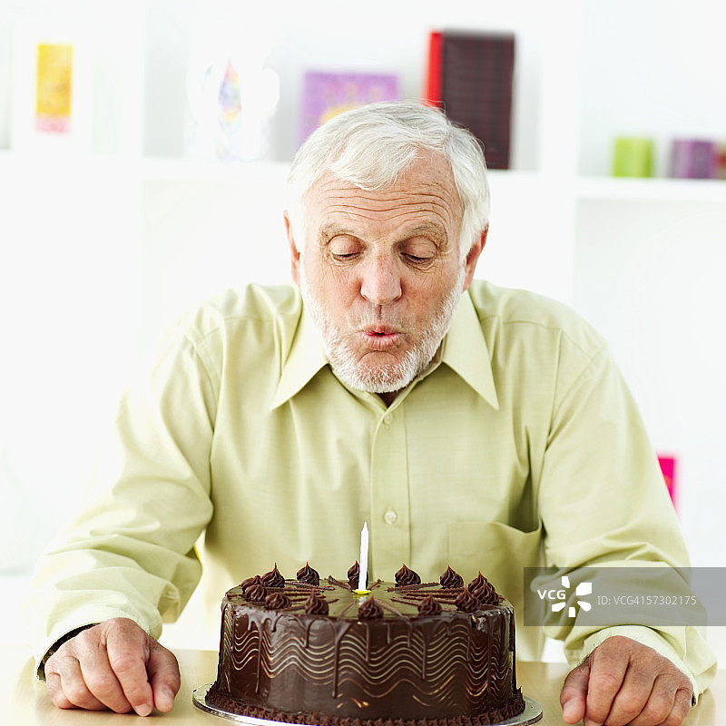 一位老人吹灭生日蛋糕上的蜡烛的肖像图片素材