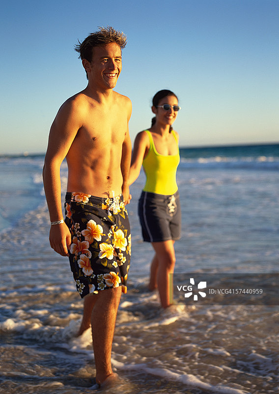 一对年轻夫妇手牵着手在海滩的水里散步图片素材