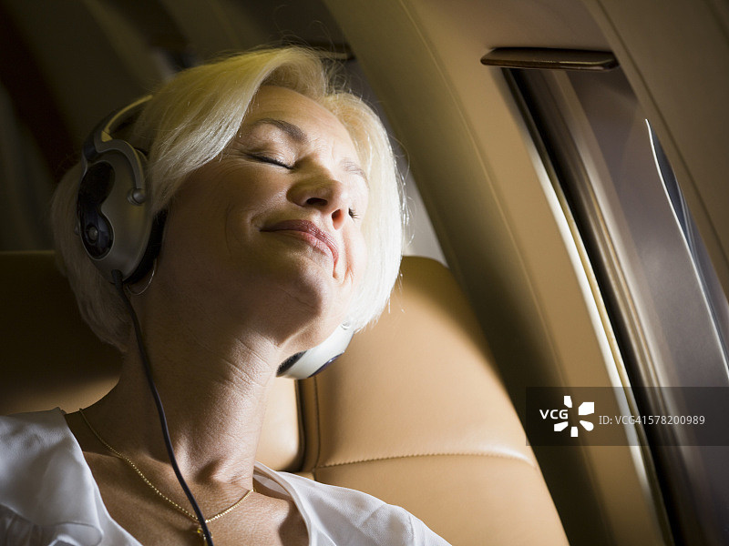 年长妇女戴着耳机，在飞机上睡觉的特写图片素材