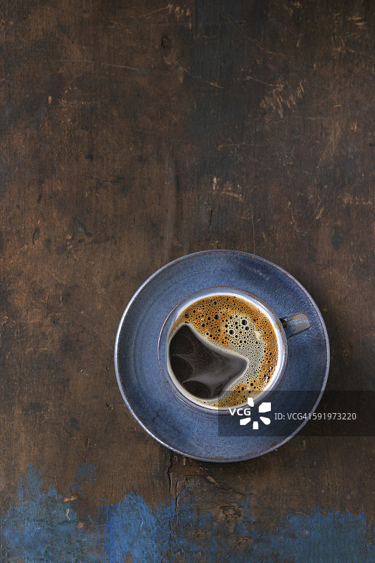 蓝色陶瓷杯黑热咖啡碟，在古老的木质纹理背景。简单的简约风格。前视图。本空间图片素材