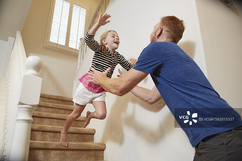 在家里的楼梯上，女孩跳进爸爸的怀里图片素材