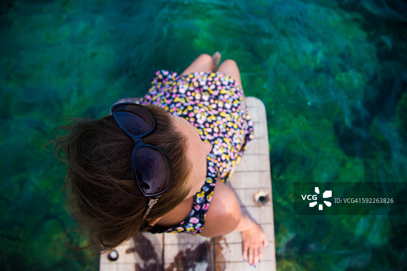 女孩坐在海滩码头上，脚在水面上沉思地中海科斯塔布拉瓦在夏天与头顶的观点。图片素材