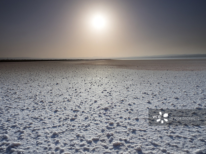 这是一个咸干湖的河床景观，有盐的形成和天空中的太阳图片素材