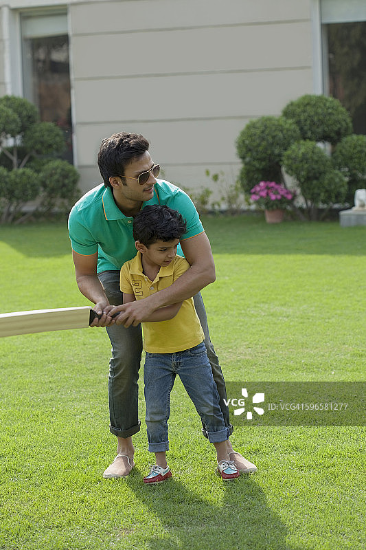 印度，父亲教小男孩(4-5岁)在后院打板球图片素材