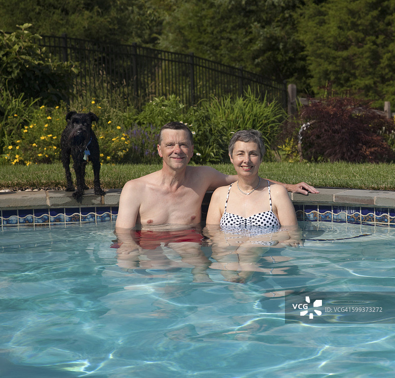 一对中年夫妇和他们的狗在家里的游泳池里放松图片素材