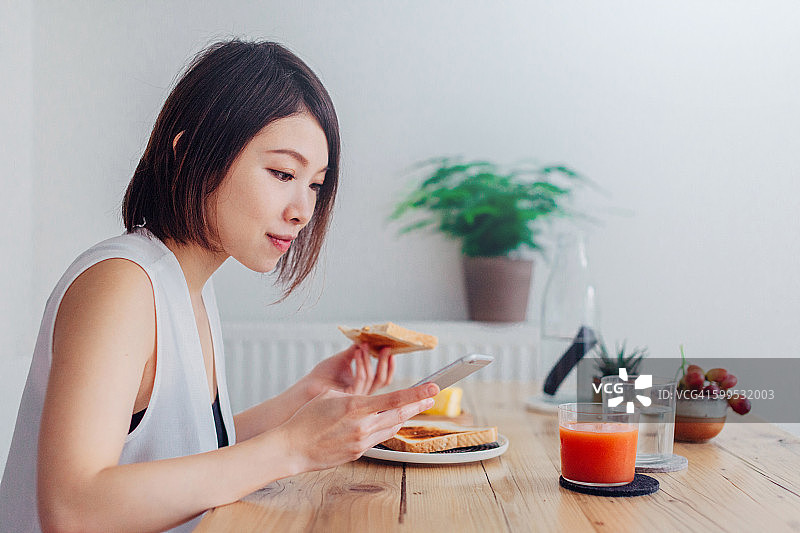 一位年轻女士在吃早餐时使用智能手机图片素材