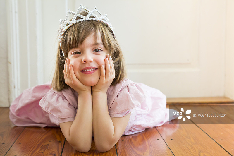 微笑的小女孩打扮成公主躺在木地板上的肖像图片素材