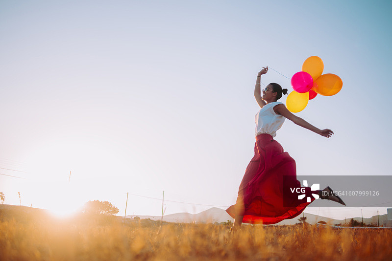 年轻女子拿着气球跑向田野图片素材
