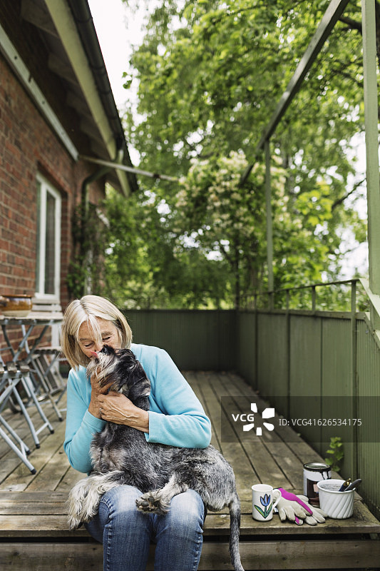 坐在门廊上亲吻狗的快乐老女人图片素材