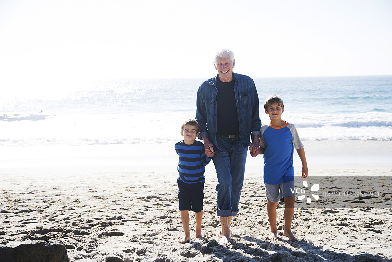 爷爷带着两个孙子，在海滩上散步，面带微笑图片素材