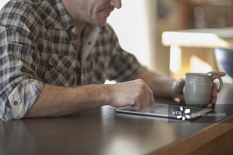 中年男人在厨房柜台边喝着咖啡边用平板电脑工作图片素材