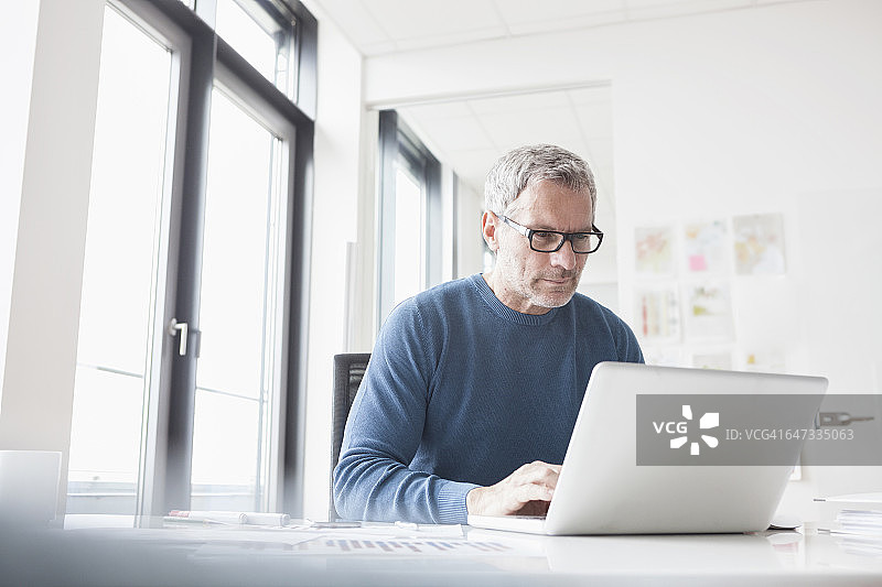 一个成熟的男人坐在办公室里用笔记本电脑图片素材