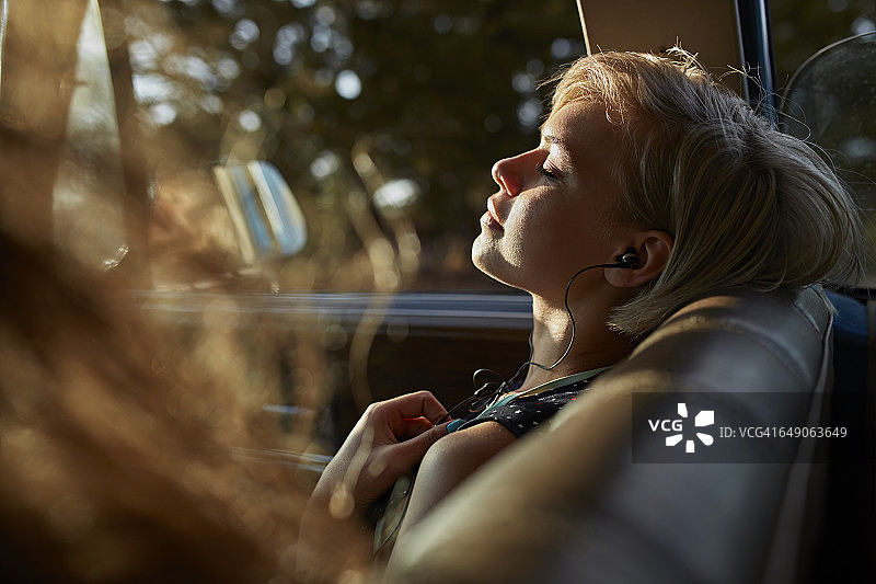 女人戴着耳机在车里放松，夕阳西下图片素材