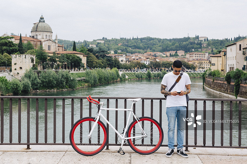 意大利，维罗纳，一个年轻人骑着自行车站在桥上图片素材