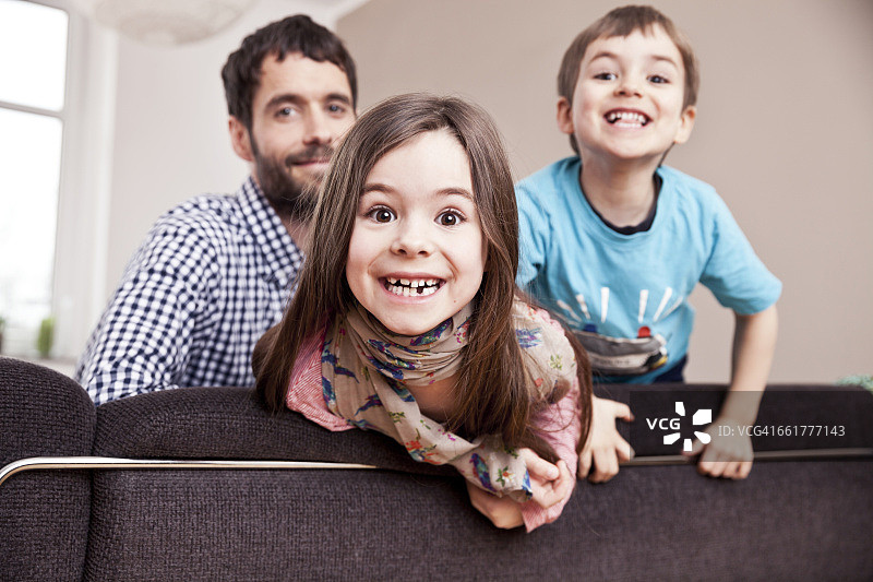 在父亲和哥哥的背景下，一个微笑的小女孩在家的肖像图片素材