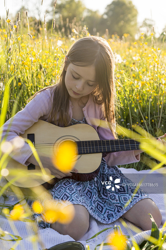 小女孩在花地上弹吉他的肖像图片素材