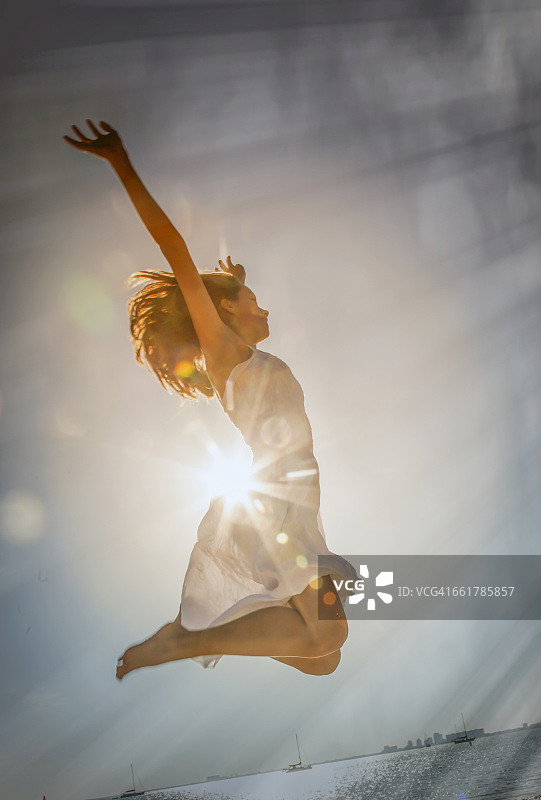 一名年轻女子在日落时分在美国佛罗里达州迈阿密海滩的半空中跳跃图片素材