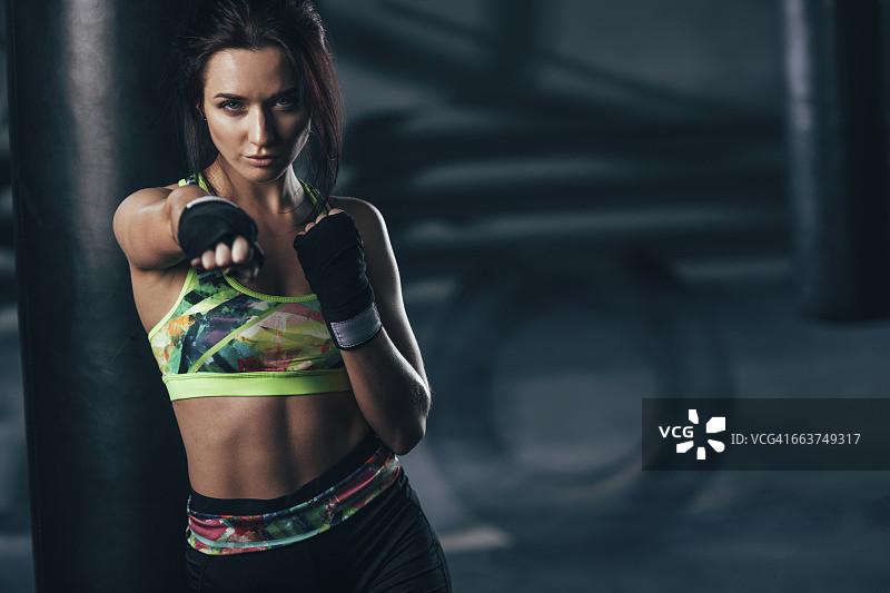 肖像坚定的拳击手摆姿势的拳击袋在健身房图片素材