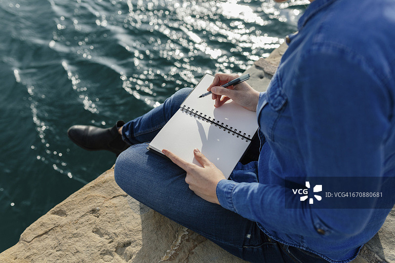 年轻女子坐在码头上写笔记本图片素材