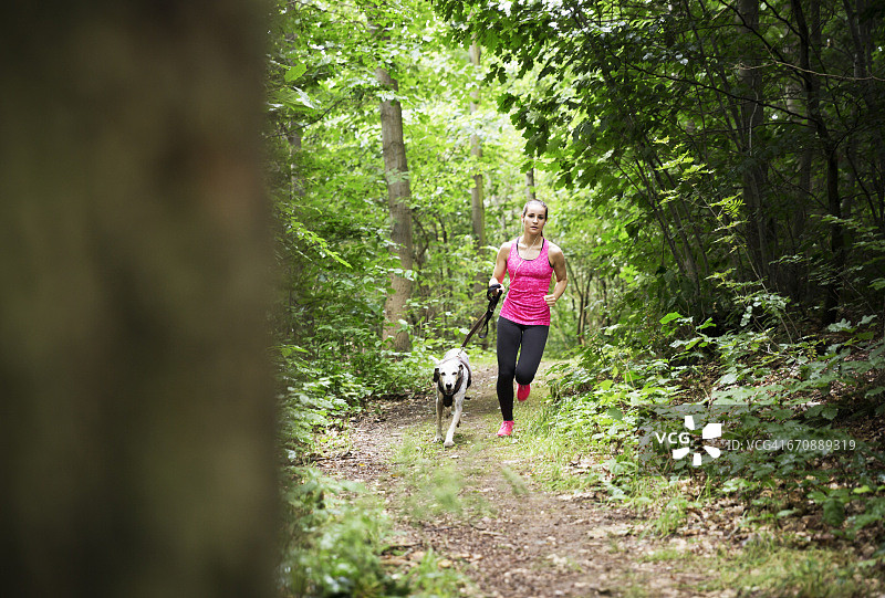 一个年轻女子带着狗在森林里慢跑图片素材