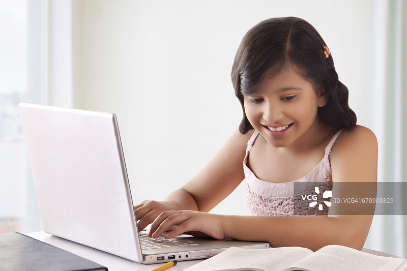 微笑的可爱女孩使用笔记本电脑的肖像图片素材