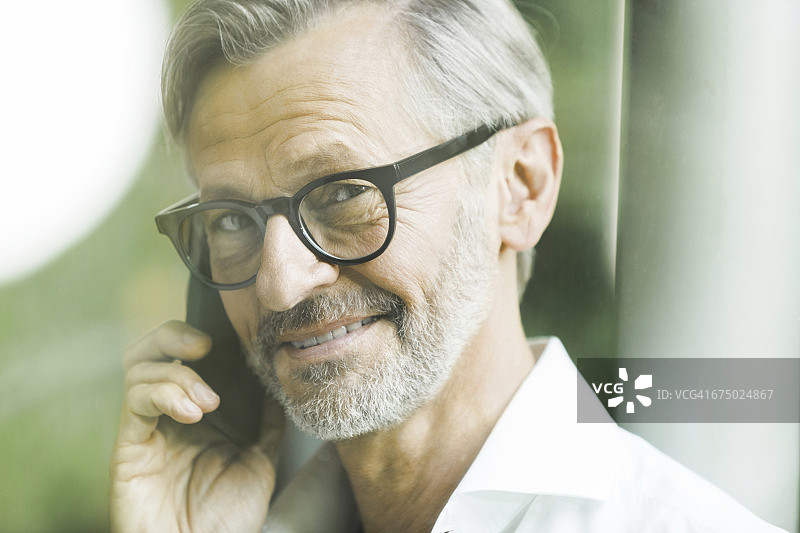 电话里一个灰色头发和胡子的微笑男人的肖像图片素材