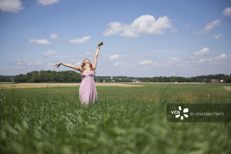 在德国巴伐利亚州的乡间草地上，快乐的女人举起双臂享受着图片素材