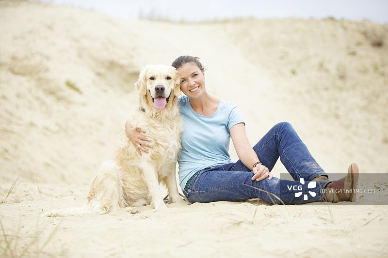 微笑的年轻女子和沙中的狗图片素材
