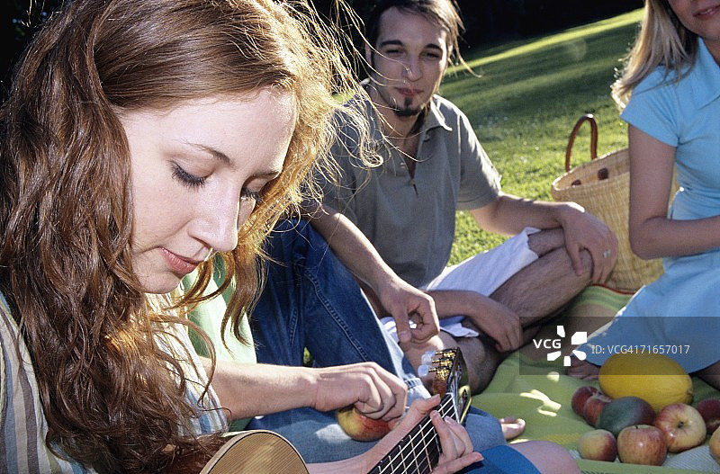 年轻女子在花园里为朋友们弹吉他，特写图片素材