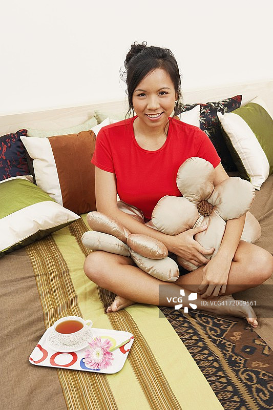 一个年轻女人的肖像坐在床上，带着垫子，微笑着图片素材