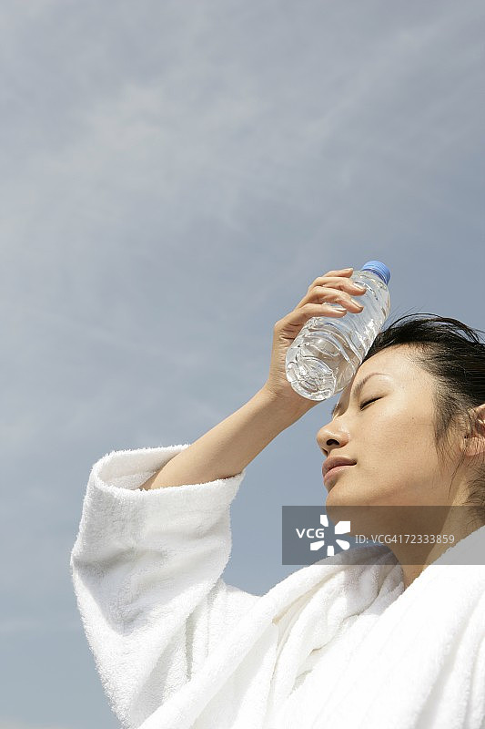一个穿着浴袍的女人把一瓶水放在额头上图片素材