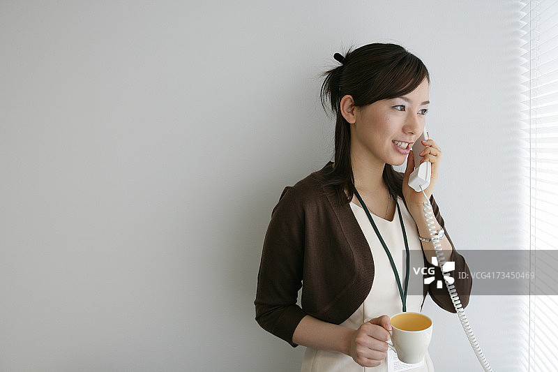 特写的一个女商人拿着一个杯子，而交谈的电话和微笑图片素材