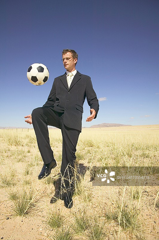 西装革履的商人在沙漠里玩足球图片素材