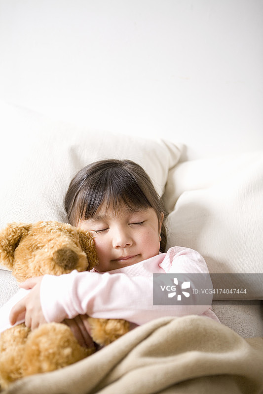 女孩(6-7)在床上睡觉，抱着泰迪熊图片素材