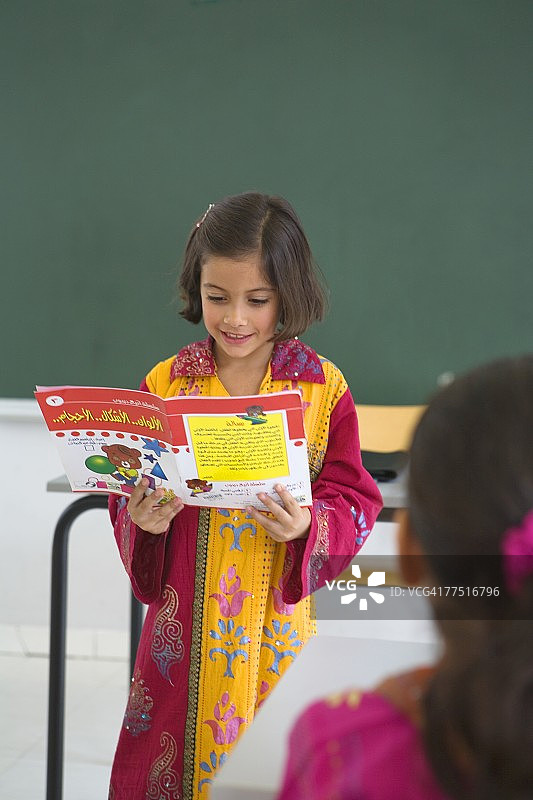 一个年轻的阿拉伯女孩在全班同学面前看书。阿拉伯联合酋长国迪拜图片素材