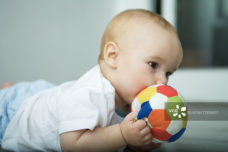 婴儿躺在地板上，把球举到嘴边图片素材