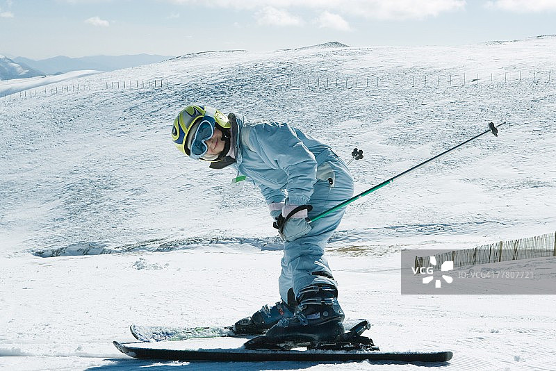 年轻的滑雪者弯下腰，对着镜头微笑，全身肖像图片素材
