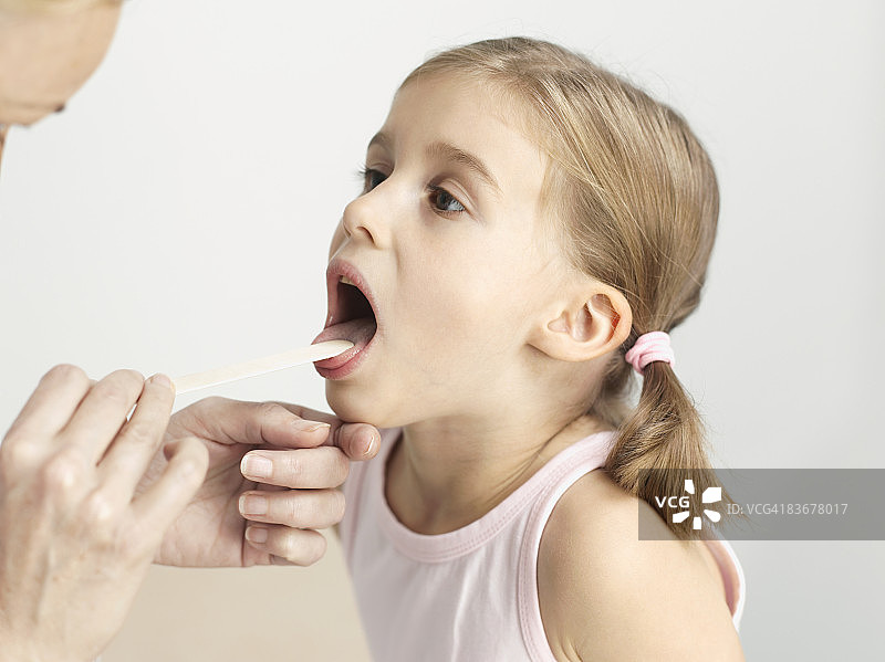 一个年轻女孩正在用压舌板检查她的喉咙图片素材