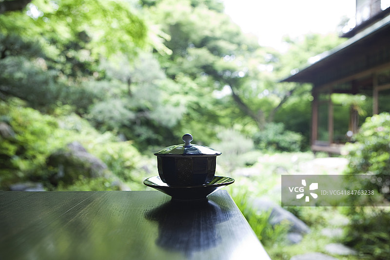 桌子上有盖茶杯和茶碟，背景是日本花园图片素材