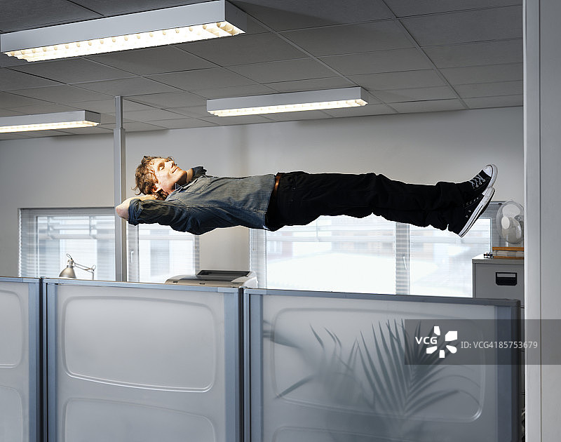 一个男人睡在他办公室桌子的上方。图片素材