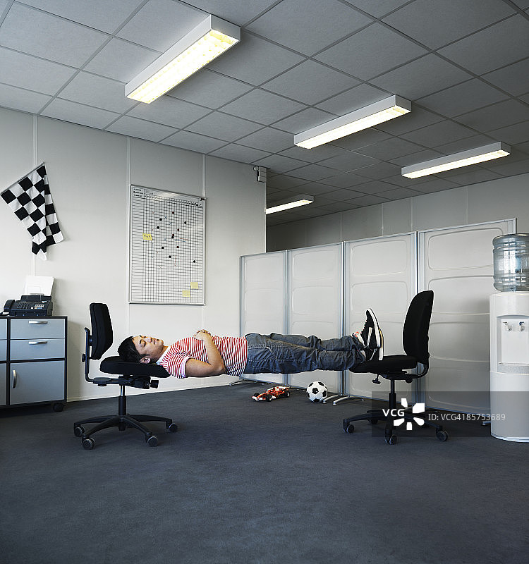一个男人睡在办公室的两把椅子上。图片素材