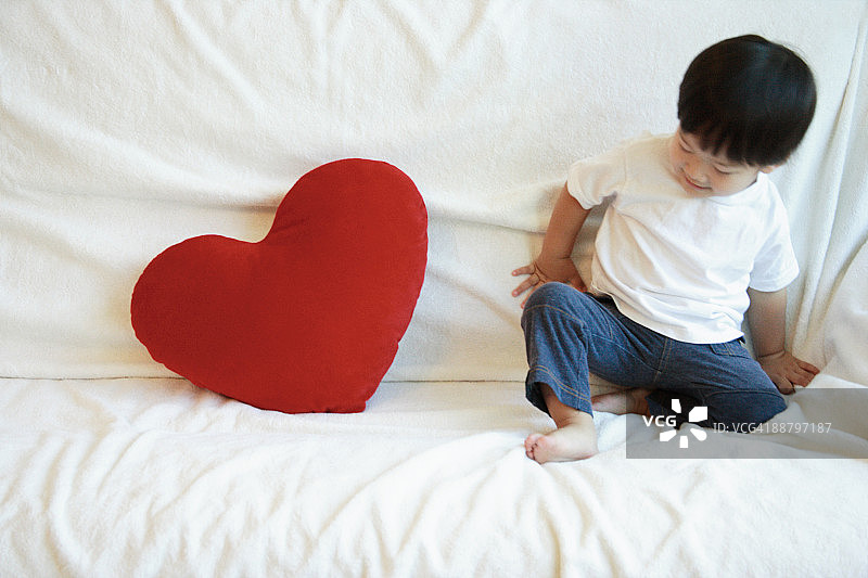 男孩坐在床上，拿着一个心形的枕头图片素材