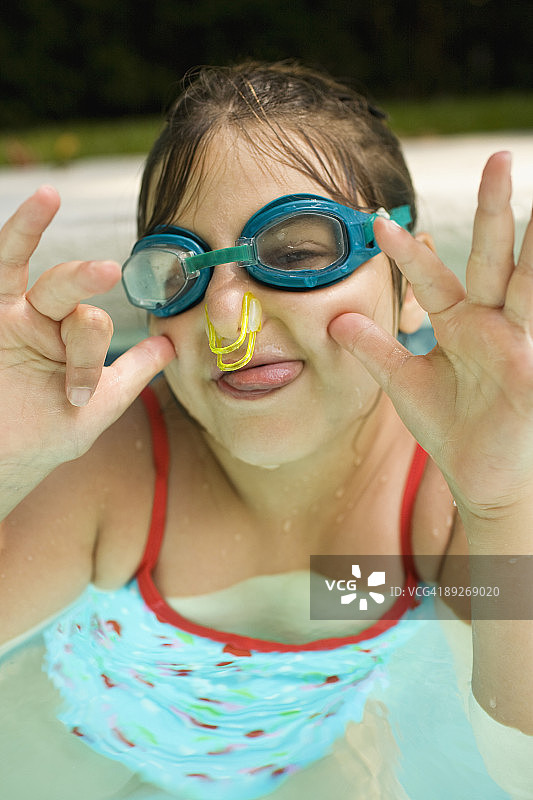 泳池里的小女孩戴着鼻塞和护目镜。图片素材