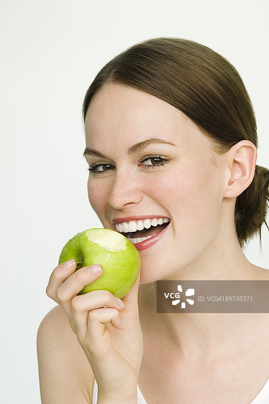 年轻女子吃着青苹果，微笑着图片素材