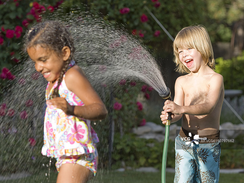 一个小男孩用水管喷一个小女孩图片素材