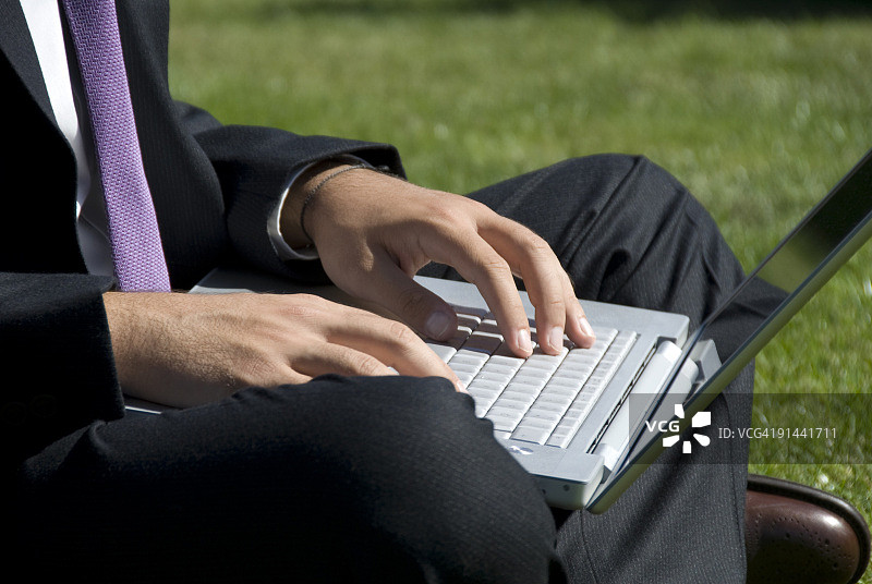 商人坐在草地上使用笔记本电脑图片素材