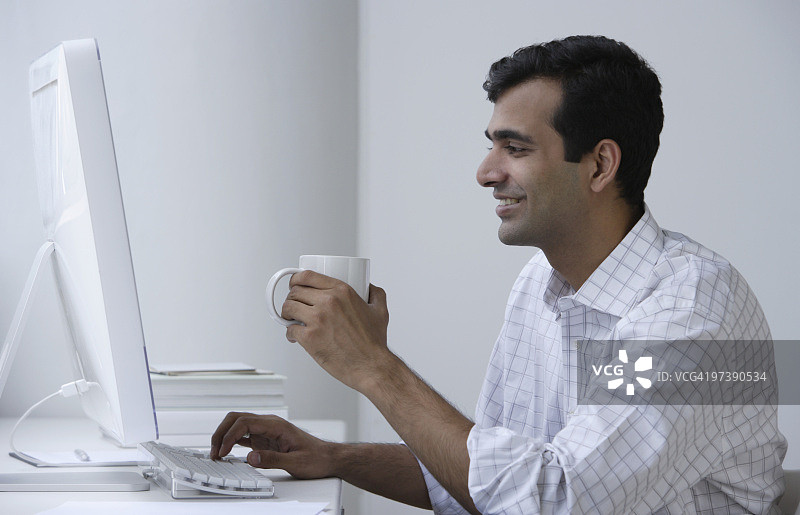 印度人在电脑前工作，喝着咖啡图片素材
