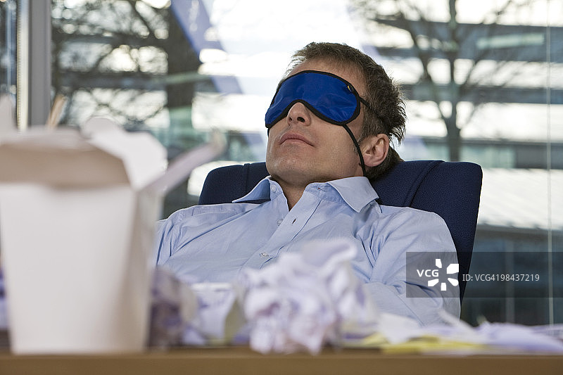 一个商人戴着睡眠面具在办公桌前打盹图片素材