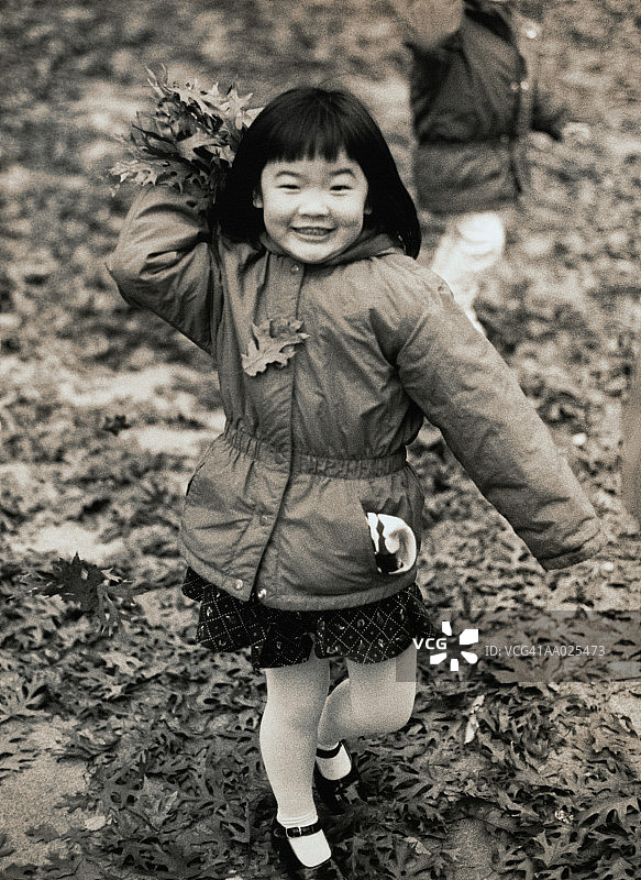 小女孩在树叶中玩耍图片素材