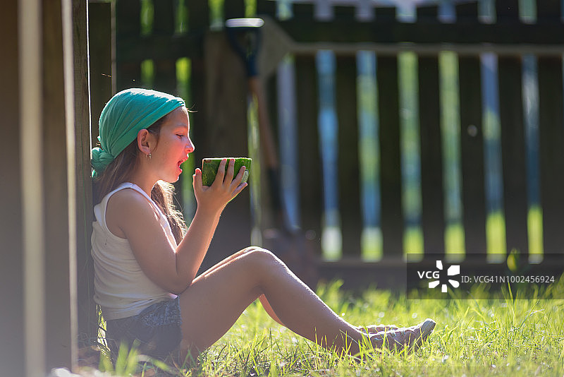 一个棕色长发的年轻女孩在户外吃新鲜的西瓜图片素材